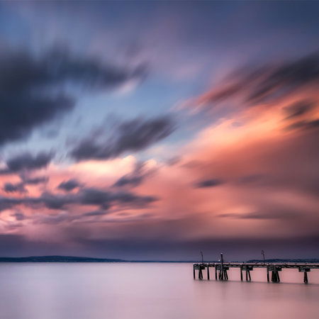         Fototapete Küstenlandschaft mit Steg im Wasser und buntem Wolkenspiel
    