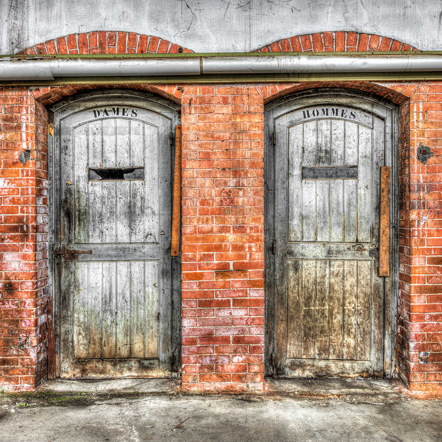             Fototapete Steinwand mit Vintage Toilettentüren – Grau, Orange, Beige
        